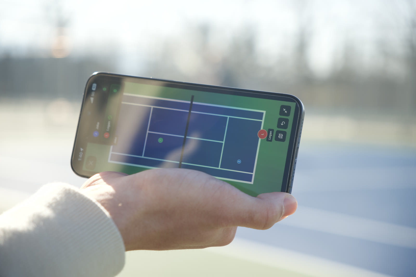 A hand holding a phone showing the live court view during a match
