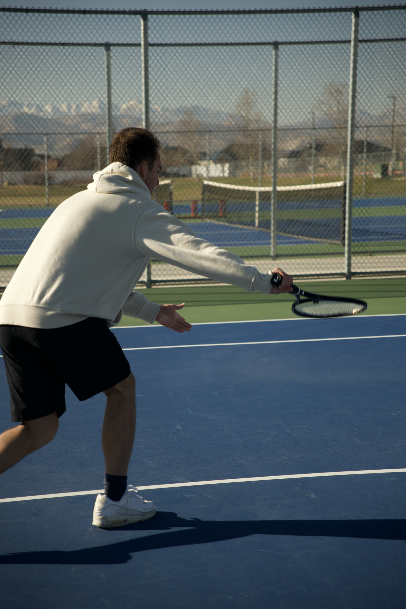 A low forehand drive with a long shadow across the court