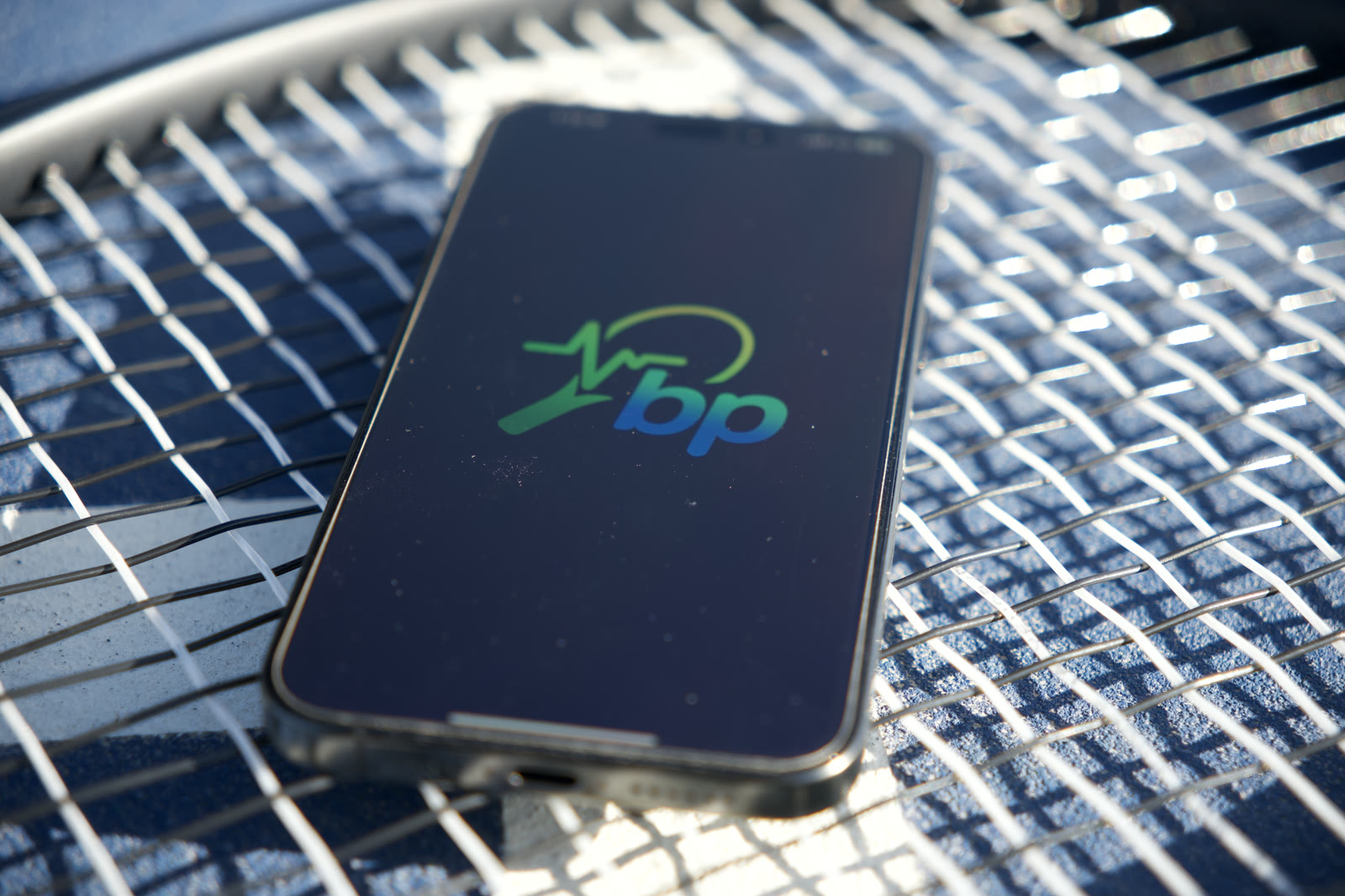 A phone resting on sunlit racquet strings, showing the MyBreakPoint logo